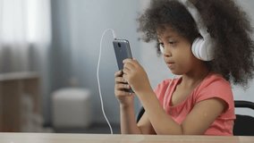 Pretty Afro-American child wearing earphones and listening to music on cellphone