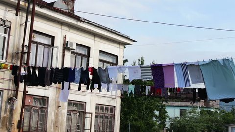 A large number of washed laundry hangs on a rope and dries on the street near the house