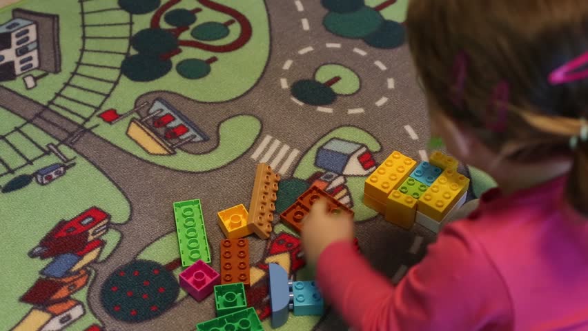 Child little girl playing wooden and plastic toys at home or kindergarten. Colorful carpet.