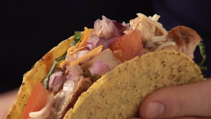 Hand holding taco shell filled with chicken