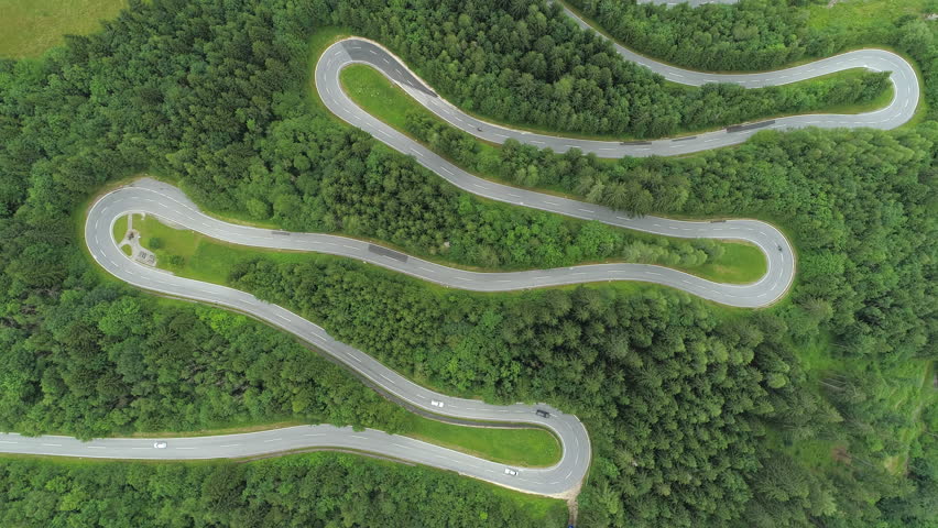 AERIAL, TOP DOWN: Motorcycles and cars driving on zig zag winding road through lush dense spruce forest on mountain slope. Curvy switchback highway with hairpin turns snaking through the woods Royalty-Free Stock Footage #31571674