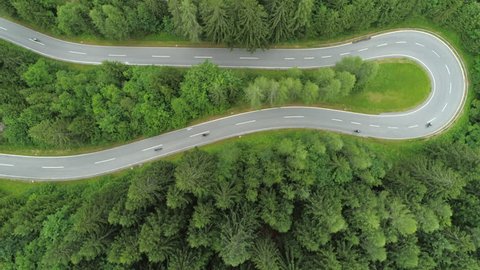AERIAL, TOP DOWN: Bikers on motorcycles speeding through sharp turns on winding zig zag serpentine road. White car driving on winding undulating mountain highway in beautiful lush green spruce forest
