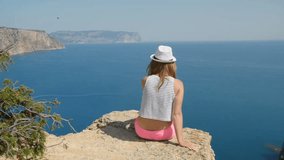 Young girl does photo near to the blue sea sitting on a mountain