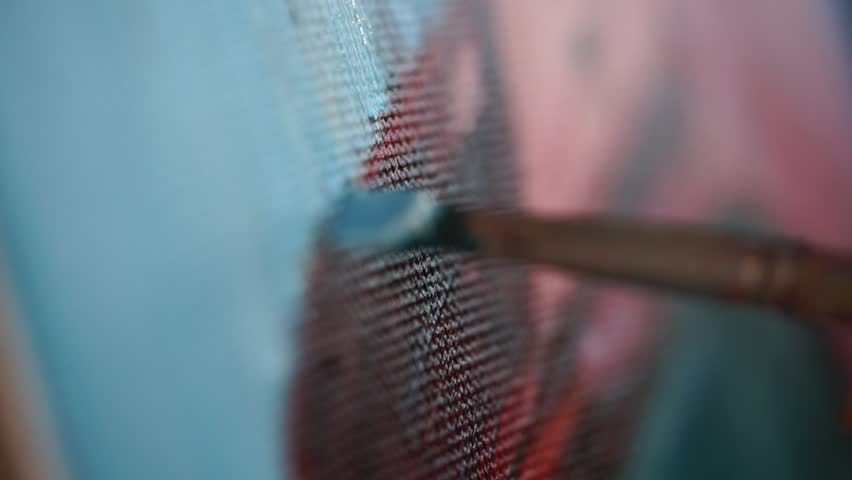 Close up shot of the process of drawing oil paints, the artist draws a line with a brush on the canvas, on the tool is a blue hue of paint