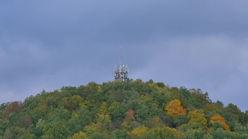 Windy weather in the forest. Strong wind removing colorful leaves from autumnal trees on forest hill.  Dark clouds move quickly across the sky. Autumn weather. 