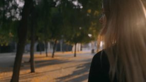 Atmospheric slow motion video of young beautiful blonde woman running towards sunset light in morning or evening park, light beams go through her hair that blows in wind