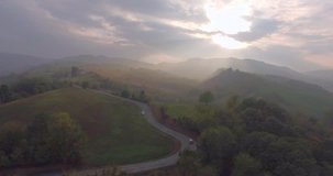Breathtaking aerial drone footage: Flight over autumn trees, meadows in sunset soft light and haze. Majestic landscape, flying over rolling hills and winding road in Italy. Beauty world.