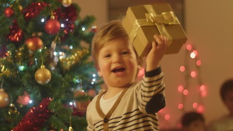 Adorable little baby boy having fun on a christmas eve at home, smiling and running around with a christmas present.