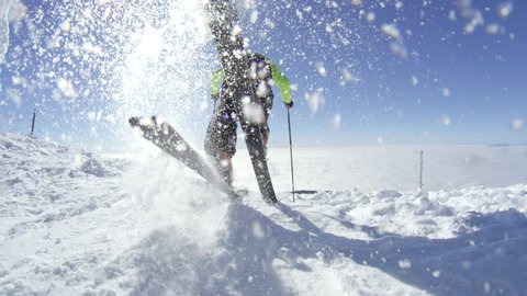 SLOW MOTION WIDE: Skier starts a ski race on a sunny winter day at top of the mountain. Spraying snow in the camera on a cloudless sunny winter day above the fog bellow in valley
