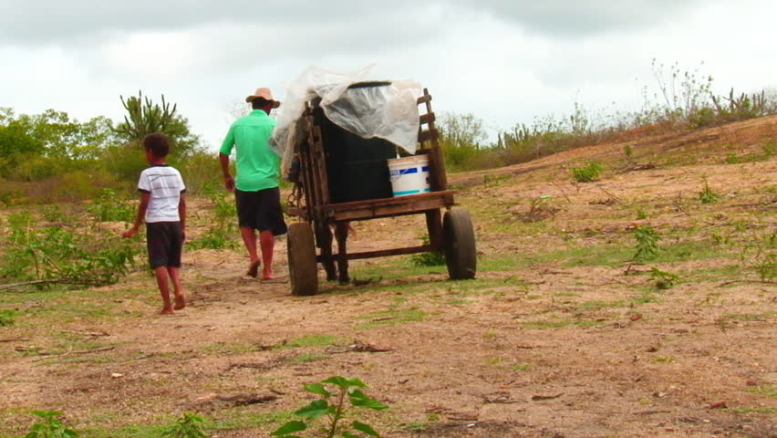 A man and his son walk away from the camera with their cart of barrels pulled by a