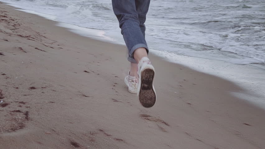 A beautiful, happy girl runs along the ocean shore. Legs close-up of rapid. on a warm autumn day