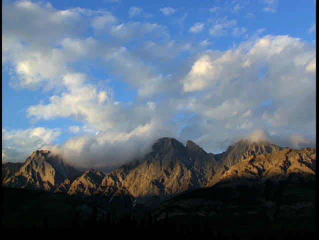 Wide shot of fluffy clouds passing over rugged Opal Mountain range in Kananaskis