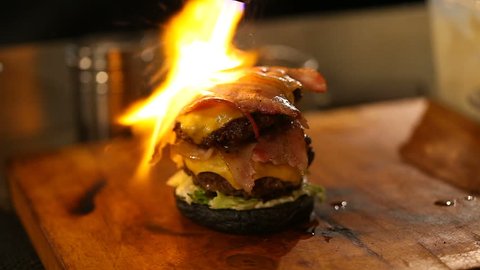 Cook uses a blow torch on a burger.