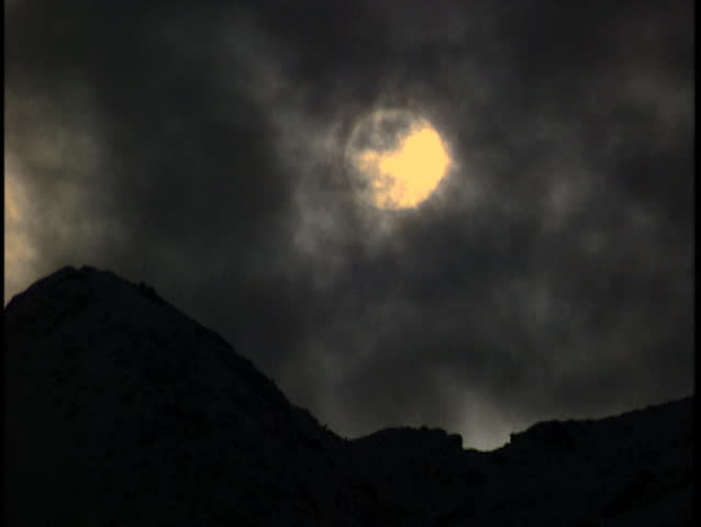 Sun setting on mountain ridge obscured by clouds