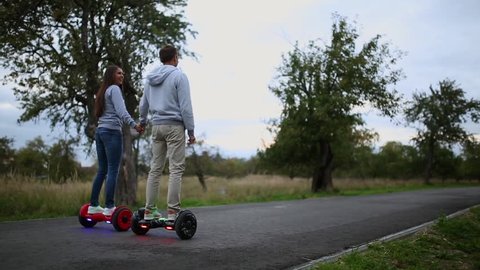 young man and woman riding on the hoverboard in the park. content technologies. a new movement. 
