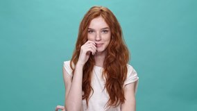Laughing ginger woman in t-shirt looking at the camera over turquoise background