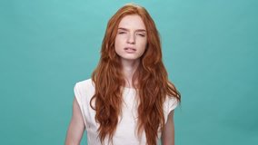 Pretty ginger woman in t-shirt with poor eyesight scrutinized at the camera over turquoise background