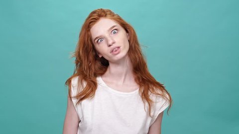 Happy funny ginger woman in t-shirt showing grimaces at camera over turquoise background
