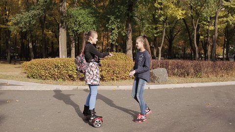 two girlfriends riding on an electronic scooter in an autumn park