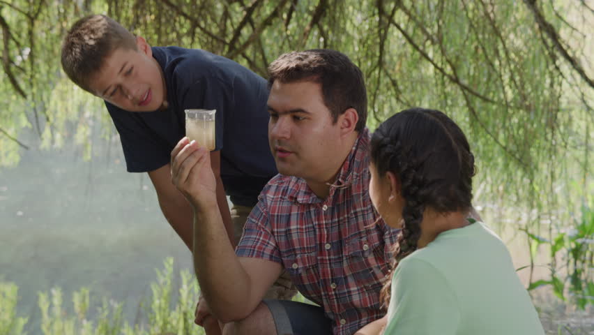 Kids at outdoor school look at cup of pond water with teacher
