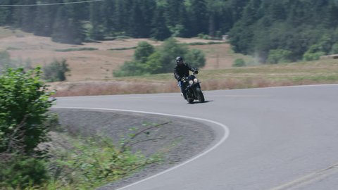 Tracking shot of man riding motorcycle on country road. Fully released for commercial use.