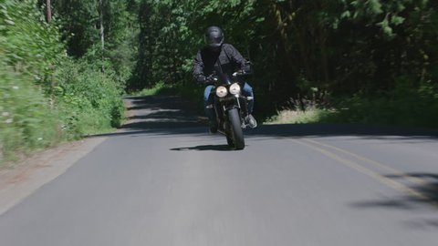 Tracking shot of man riding motorcycle on country road. Fully released for commercial use.