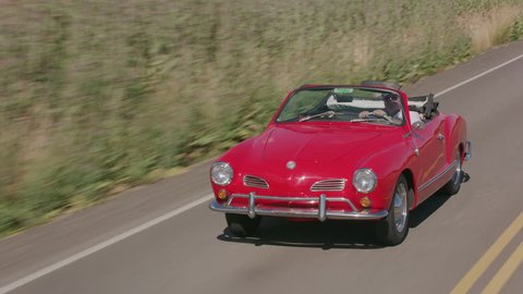 Tracking shot of man driving classic convertible car on country road. Fully released for commercial use.
