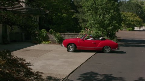 Tracking shot of man pulling out of driveway in classic convertible car. Fully released for commercial use