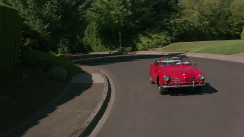 Tracking shot of man driving classic convertible car through neighborhood. Fully released for commercial use.