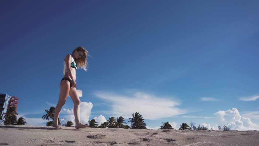 girl in bikini walking along the beach with sand