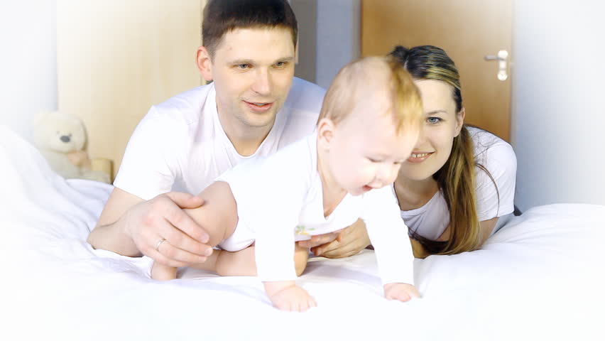 Happy family: father, mother and baby playful in the bedroom