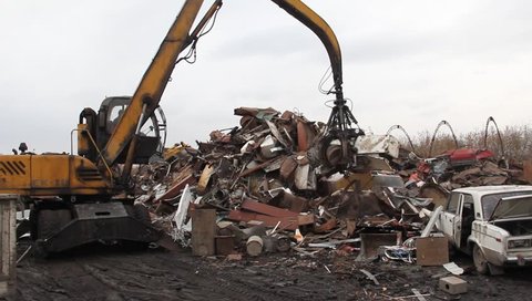 Excavator is loading scrap metal junk into a bin at a garbage dump or recycling center.