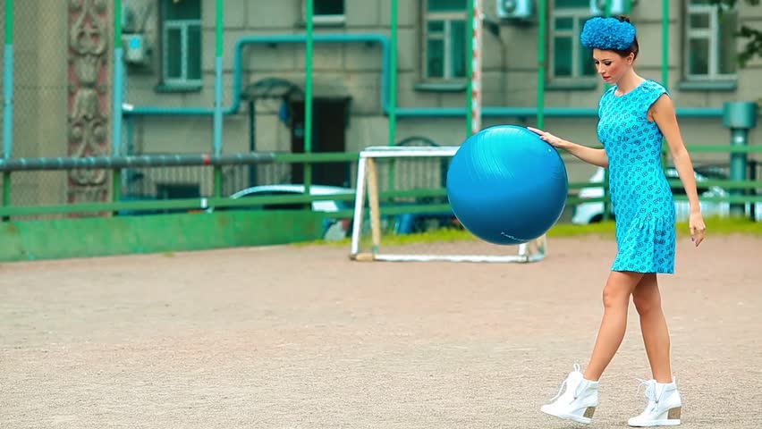 Girl in a blue dress playing with a ball in the courtyard