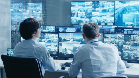 In the Security Control Room Two Officers Monitoring Multiple Screens for Suspicious Activities, They Report any Unauthorised Activities. They Guard Object of National Importance. 4K UHD.