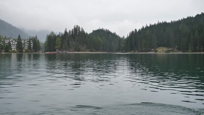 Young casual man sitting in wooden boat and rowing while looking away on background of lake and mountains.