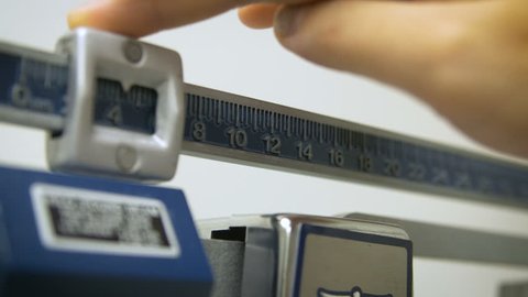 A hospital nurse is adjusting the numbers on the weight scale very slow with her