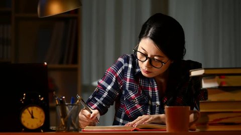 Young woman doing homework at night. Tired hispanic girl and college education. Female student studying for next day exam. mixed race asian chinese model.