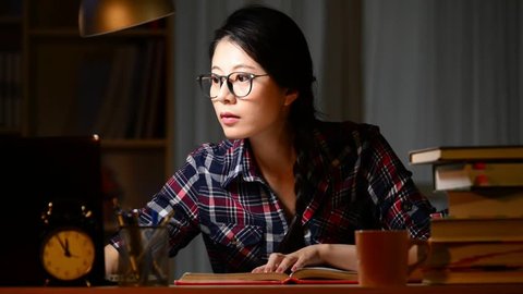 Concentrated asian young woman in glasses using computer for studying and writing in the evening at home. mixed race asian chinese model.