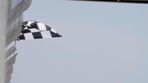 Man holding and waving Checkered race flag in slow motion at finish line on a raceway. Victory, achievement, success and sport concept.