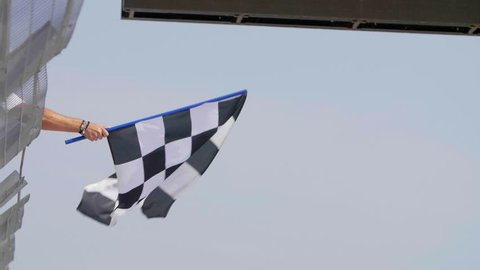 Man holding and waving Checkered race flag in slow motion at finish line on a raceway. Victory, achievement, success and sport concept.