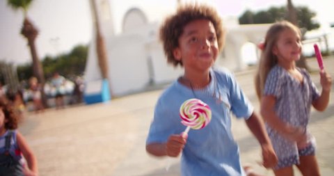 Multi-ethnic kid friends having fun running with colorful candy on summer holidays