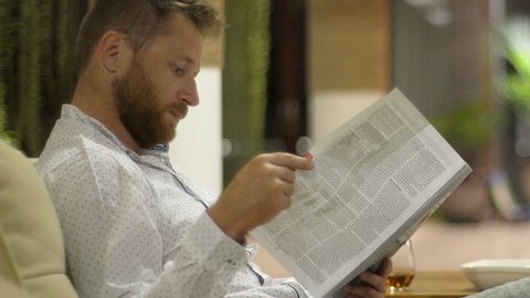 Man reading magazine and drinking whiskey while relaxing in his flat
