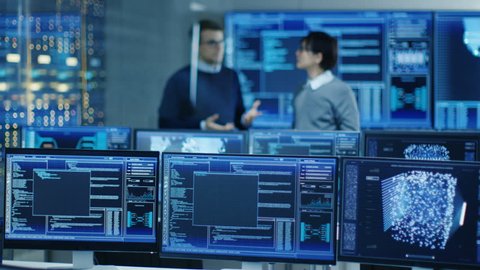 In the Data Center System Control Room Monitors Show Work Done on Neural Networking, AI integration and Data Mining. In the Background Two Specialists Talking. Shot on RED EPIC-W 8K Helium Camera