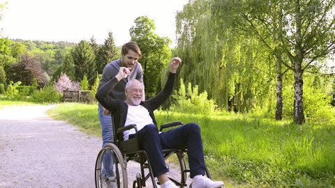 Son with disabled father in wheelchair in the park.