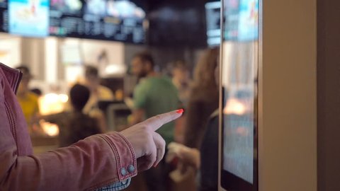 Woman choosing dessert via self-service machine at fast food restaurant. Girl using touch terminal im Mcdonalds makes a quick order through the self-service. Person swipes the screen making an order.