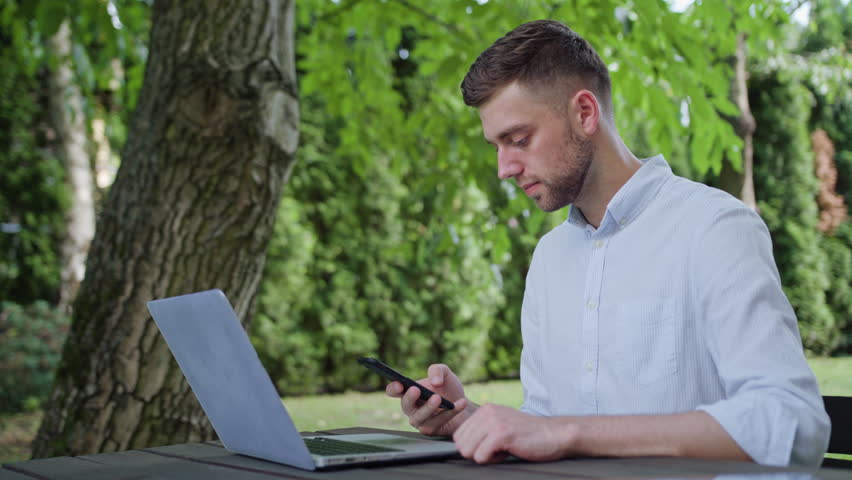 A young man using a phone in the park and sitting at the table. Medium shot. Soft Focus