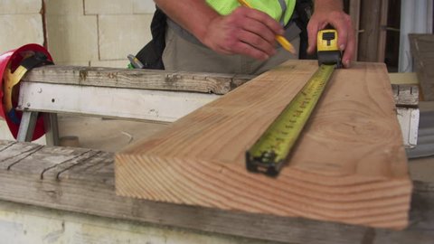 Construction worker measuring and marking lumber