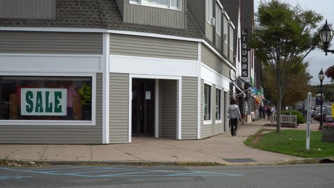 Generic corner clothing store in small town USA America day time exterior establishing shot. Unrecognizable people walk sidewalk on Main Street in distance