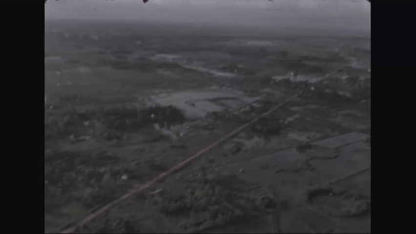 CIRCA 1960s, 1970s - A flet of UH-1D helicopters fly above fields firing below, and land along a road, during the Vietnam War.