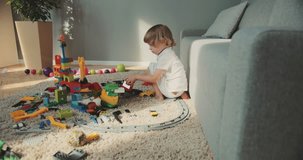 Little cute boy sitting floor and enjoying toys at home. Baby designer game baby playing focused at home family curly hair colored toys lego designer cars children's track. Contemporary design.